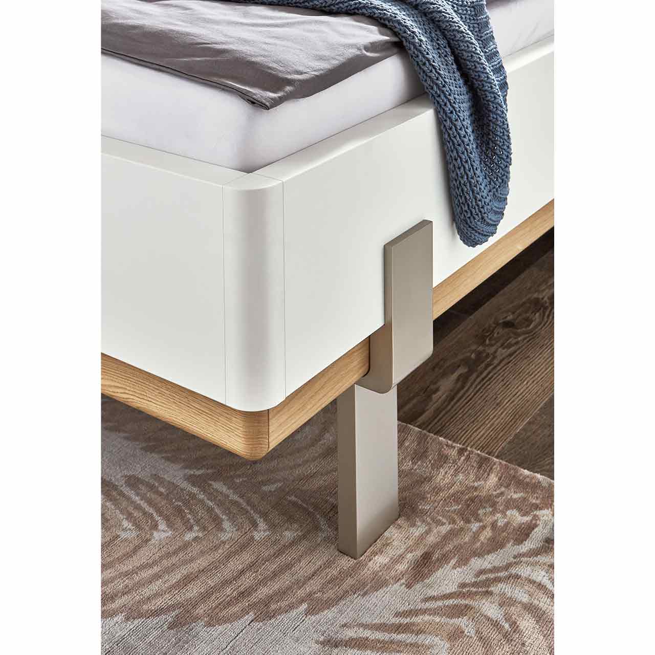 wsl6000-bett-detail Bett Detailansicht, seitlich das Bett hat abgerundete Kanten in Lack weiß kombiniert mit Wildeiche Akzent im unteren Bereich als Abschlusskante, die silberfarbigen Metallfüße schmiegen sich an der Bettkorpus.