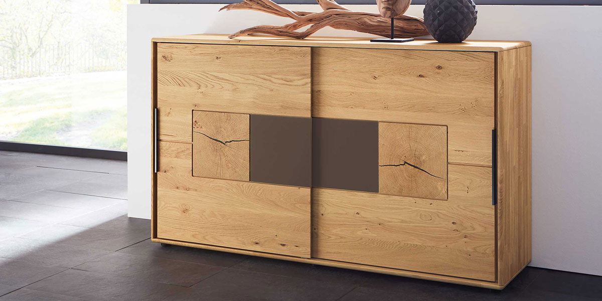 Wöstmann Kommoden Banner zeigt Kommode 2167 in Wildeiche, mit platzsparende Schiebetüren mit Hirnholz und Lack Mocca Akzent. Bringen Sie Eleganz und Ordnung in Ihr Schlafzimmer mit einer Wöstmann Kommode.