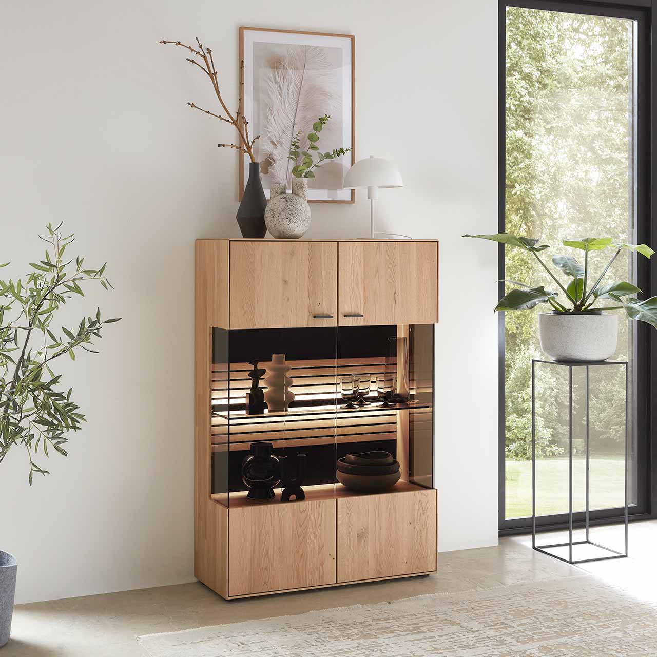 WM 2320 Highboard 4940 Modernes Highboard aus Wildeiche mittig mit Vitrinenfach und Glasboden. Das absolute Highlight ist die Rückwand, eine Kombination aus Mattglas und aufwendigen Lamellen in der die LED Beleuchtung ein Lichtspiel erzeugt.