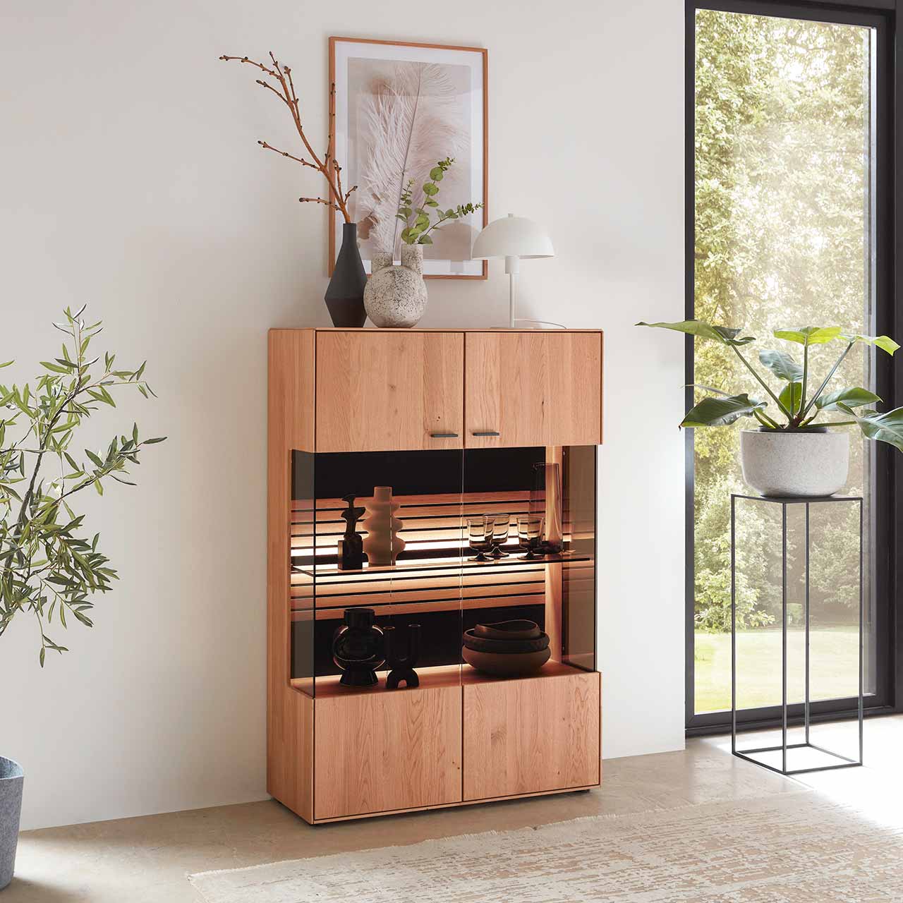 WM 2320 Highboard 4940 Erle Modernes Highboard aus Erle mittig mit Vitrinenfach und Glasboden. Das absolute Highlight ist die Rückwand, eine Kombination aus Mattglas und aufwendigen Lamellen in der die LED Beleuchtung ein Lichtspiel erzeugt.
